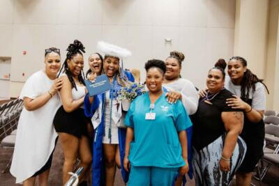 Un alegre grupo posa en un vestíbulo, celebrando un graduado con toga y birrete azul con un halo de plumas.